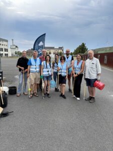 Menschen in blauen Westen halten Müllzangen und stehen in einer Gruppe zusammen