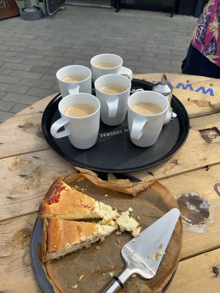 Fünf Tassen mit Kaffee stehen auf einem Tablett. Daneben steht ein Tablett mit zwei Stücken Kuchen