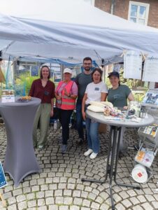Freiwillige des ach so Vereins stehen an einem Info-Stand